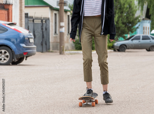 Young girl in a white T-shirt, black sweater and brown trousers learns to ride a skateboard