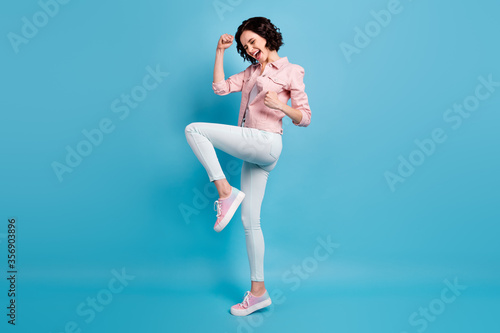 Full body profile photo of beautiful crazy lady raise hands fists celebrating goal match game football team supporter wear casual pink jacket pants shoes isolated blue color background