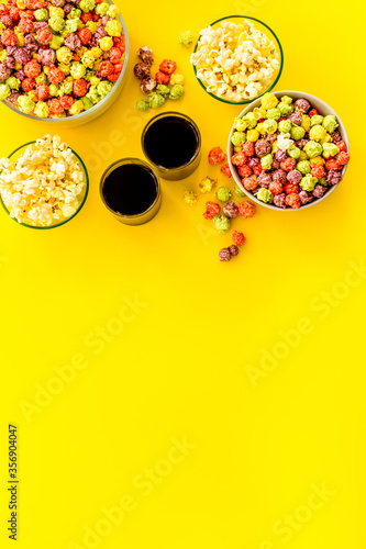 Top view of flavored popcorn and soda on yellow desk from above copy space