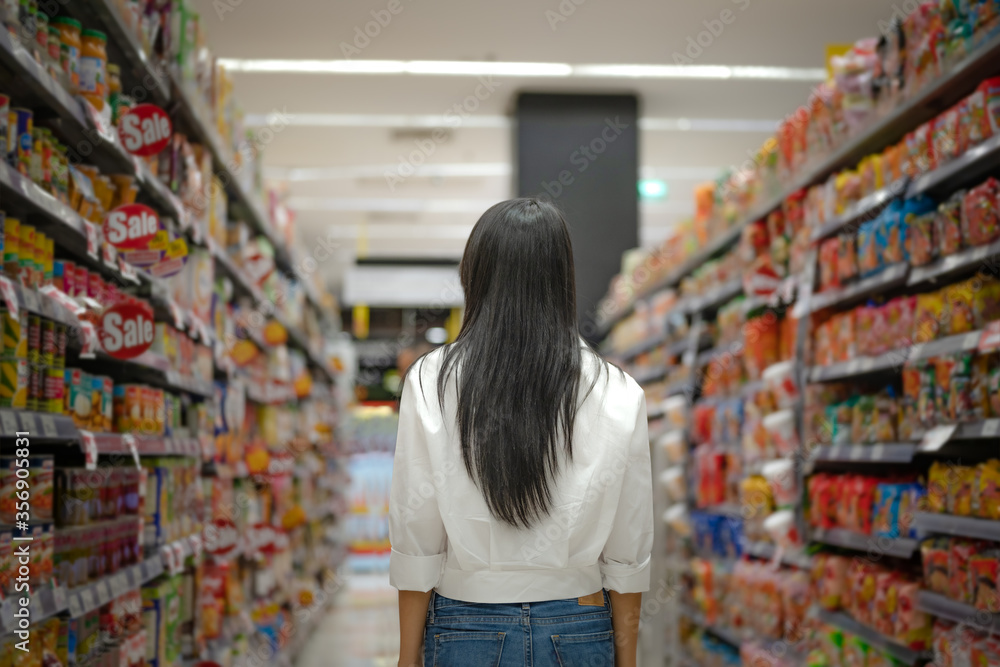 woman in supermarket grocery store walks ahead to buying daily products goods for household apply