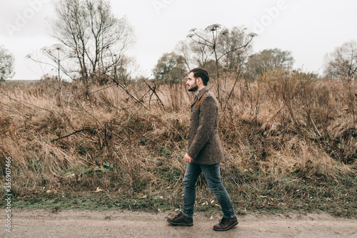 Handsome sadly young stylish man in a  jacket and jeans walks on the nature of jubilee dried autumn flowers. Cloudy weather  spring  dry grass