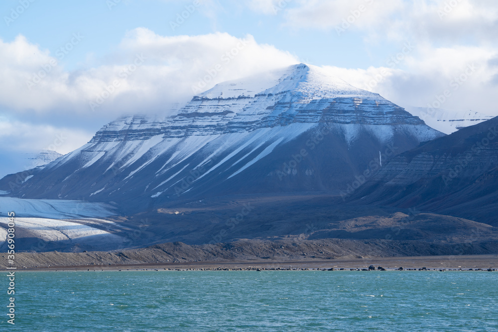Blue fjord during the Arctic summer with snow covered high mountains.
