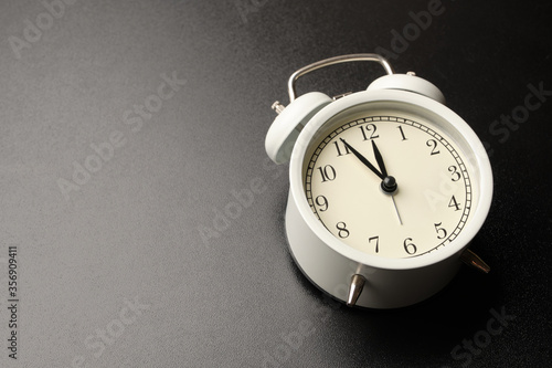 White vintage alarm clocks show almost midday or midnight isolated on black table background.