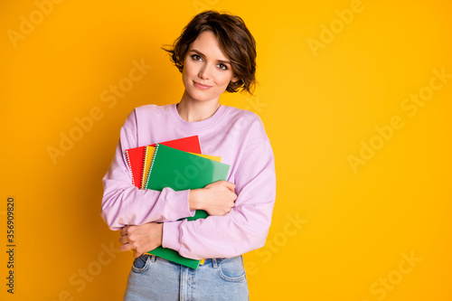 Portrait of her she nice attractive lovely pretty content cheery girl holding in hands educational materials courses classes isolated on bright vivid shine vibrant yellow color background