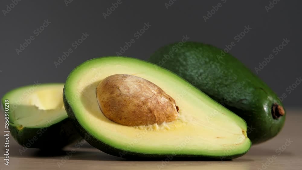 Male hands stack one natural whole avocados on the table next to the cut avocado halves with a whole bone. Freshly avocado on a table. Healthy fruit and vegetables for weight loss after self-isolation Male hands stack one natural whole avocados on the table next to the cut avocado halves with a whole bone. Freshly avocado on a table. Healthy fruit and vegetables for weight loss after self-isolation