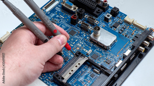 Human hand measurement with multimeter probes of the LCD TV motherboard chip. Disassembled LCD TV. Repair of consumer electronics. Electronics repairman.