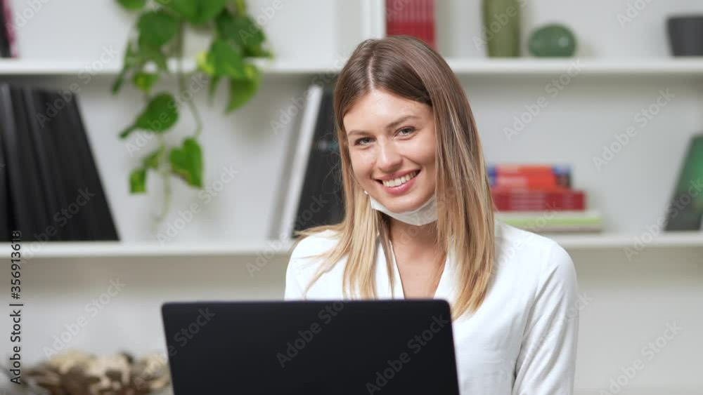young girl works at the computer in her office and takes off her mask confident for the future
