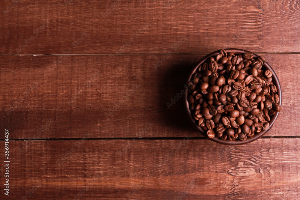 Arabica coffee beans in clay bowl on brown wooden table background. Closeup, copy space, top view. Arabica seeds, roast, caffeine concept