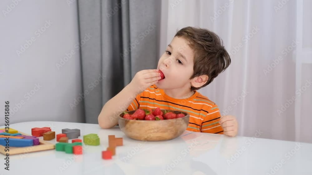 Smiling boy at breakfast eating fruit strawberries. stock footage. Slow Motion video. Close up Smiling boy at breakfast eating fruit strawberries. stock footage. Slow Motion video. Close up