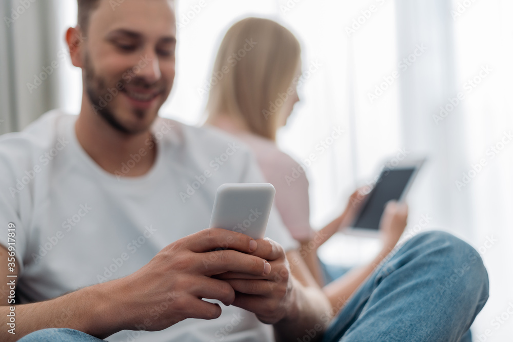 selective focus of happy man using smartphone near woman holding digital tablet selective focus of happy man using smartphone near woman holding digital tablet