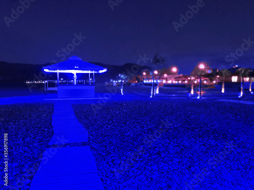 Bar with blue neon lights on the sea beach at night.