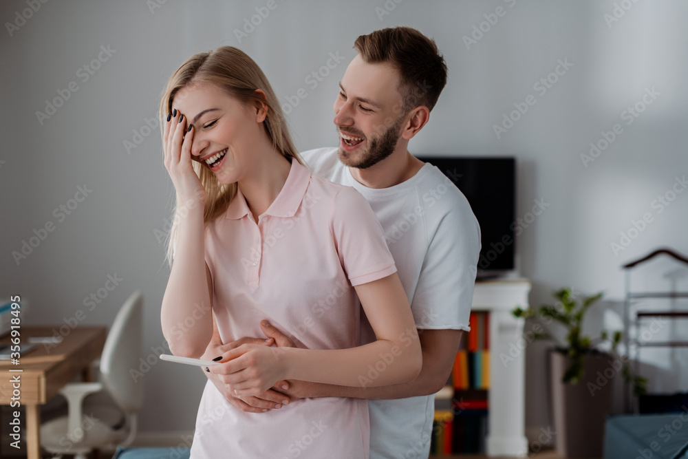 Obraz premium happy man hugging cheerful girlfriend holding pregnancy test with positive result