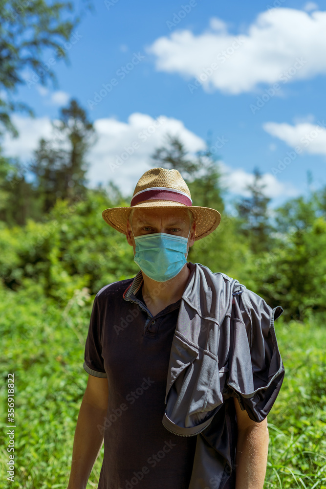 Mann über 40 mit einem Mundschutz und einem Sonnenhut im Wald, Natur, Sträucher, Corona, Selbstschutz