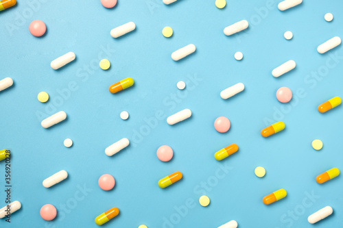Close up of many different pills arranged in pattern on blue background.