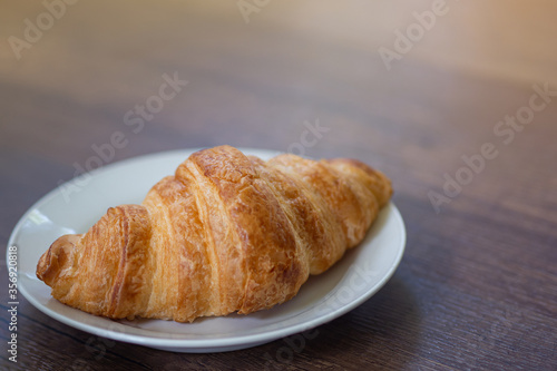 Close-up of croissant on plate placed on a wooden table. Space for text.