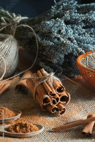 Ground cinnamon, cinnamon sticks, tied with jute rope on old straw bag background in rustic style