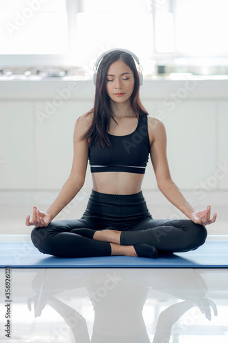 Young woman with headphone doing yoga at home.