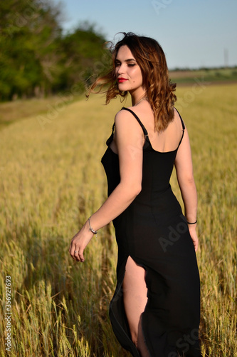 Beautiful young girl in a black sexy dress in a wheat field