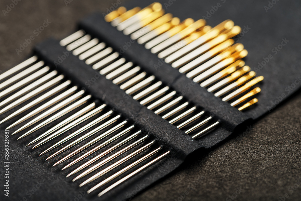 Gold sewing needles on a black background in a row. Gold sewing needles on a black background in a row.