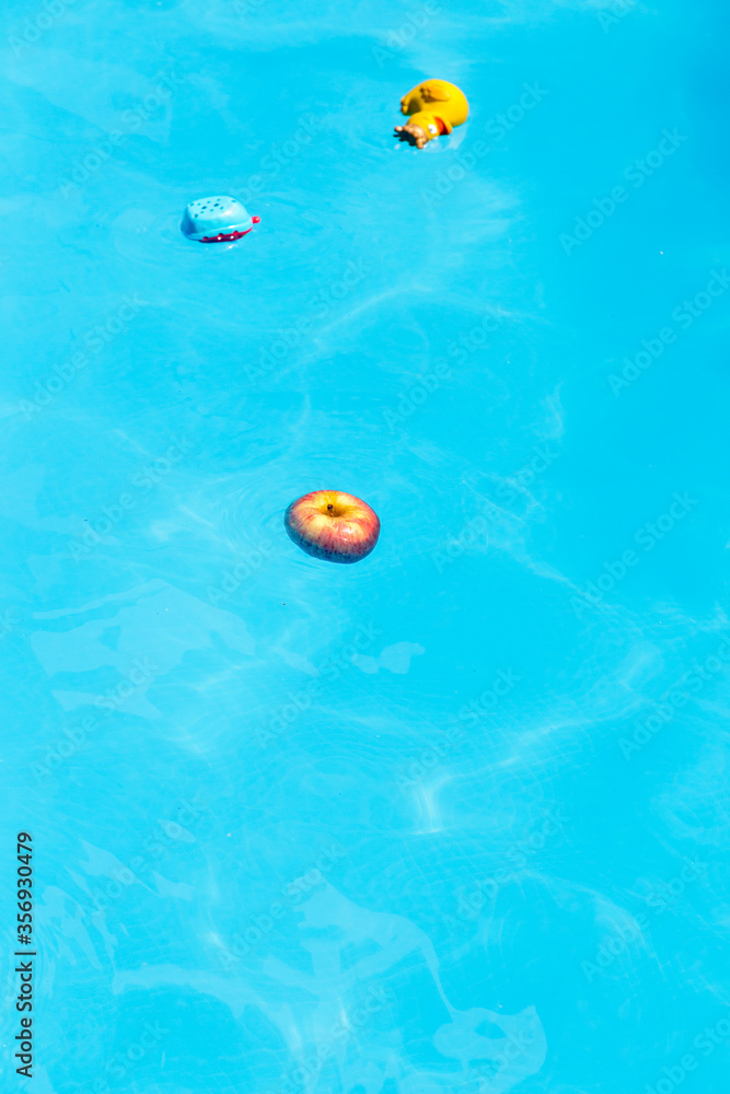 Naklejka premium apple and toys floating in the water of a pool