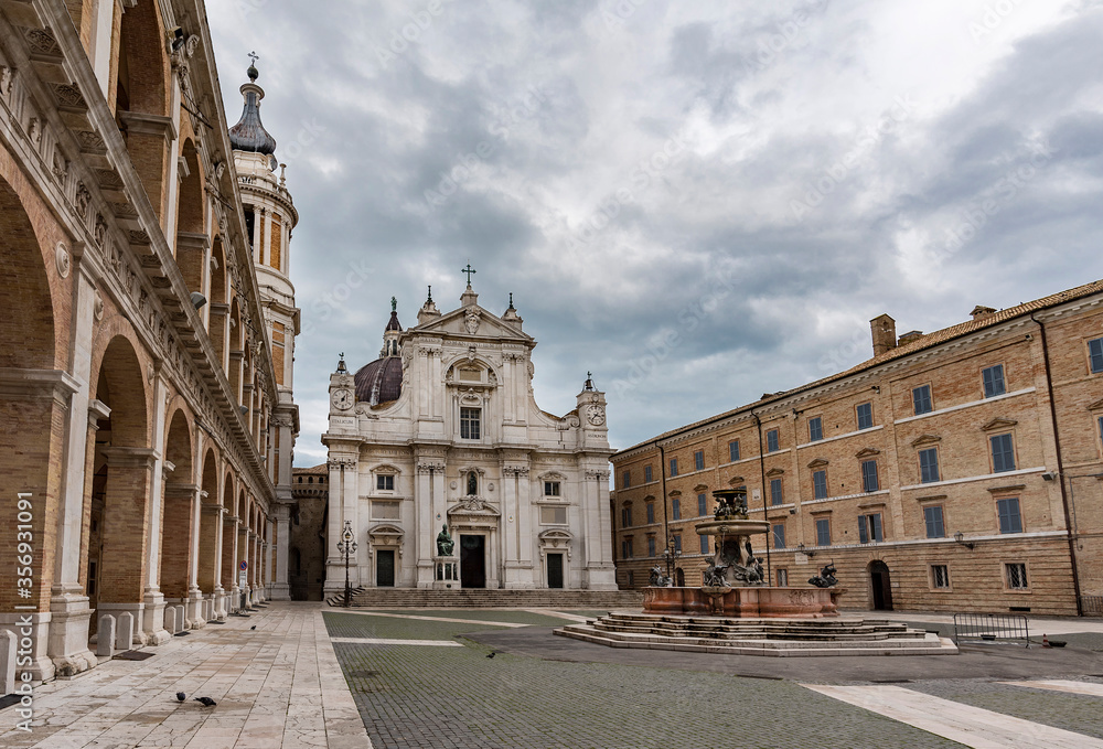 Italy, Loreto,square of Loreto with background the basilica with cloudy sky, portico to the side, perspective photo