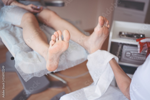 Podiatrist using grinding equipment and making procedure polish for feet pedicure. Podology beautician in white gloves cleaning skin of client legs from callus and corn with professional tool.