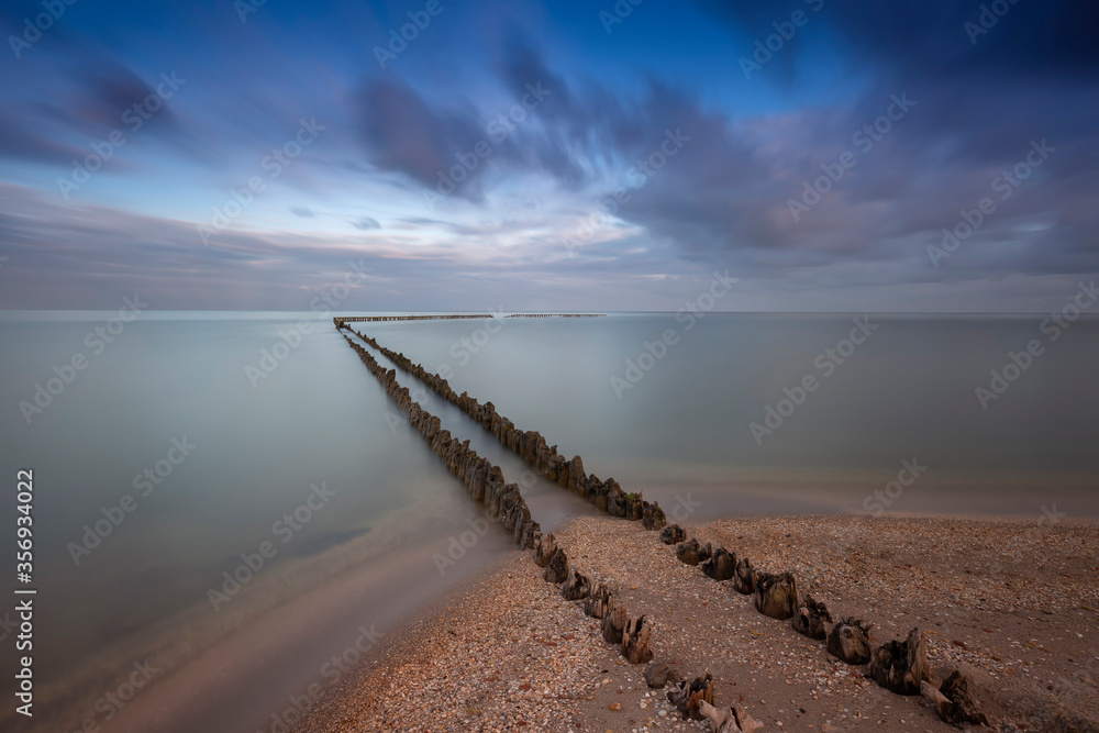 Holland - An old, dilapidated, wooden breakwater, begins on the edge of a sandy beach and ends in the sea. For a long time calmed the sea, dynamic sky. Romantic atmosphere. Holland - An old, dilapidated, wooden breakwater, begins on the edge of a sandy beach and ends in the sea. For a long time calmed the sea, dynamic sky. Romantic atmosphere.