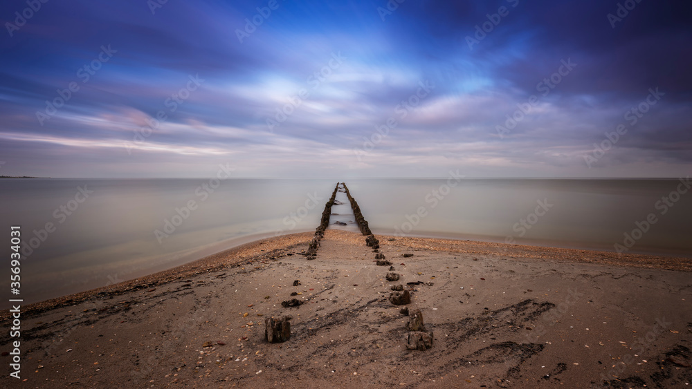 Holland - an old, dilapidated, wooden breakwater that begins on the edge of a sandy beach and ends in the sea. For a long time he calmed the sea, colored the floating clouds. Romantic atmosphere.