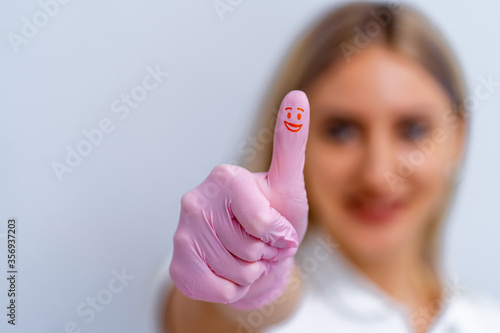 Dentist woman in pink gloves. Showing cool sign. Red smile on thumb.