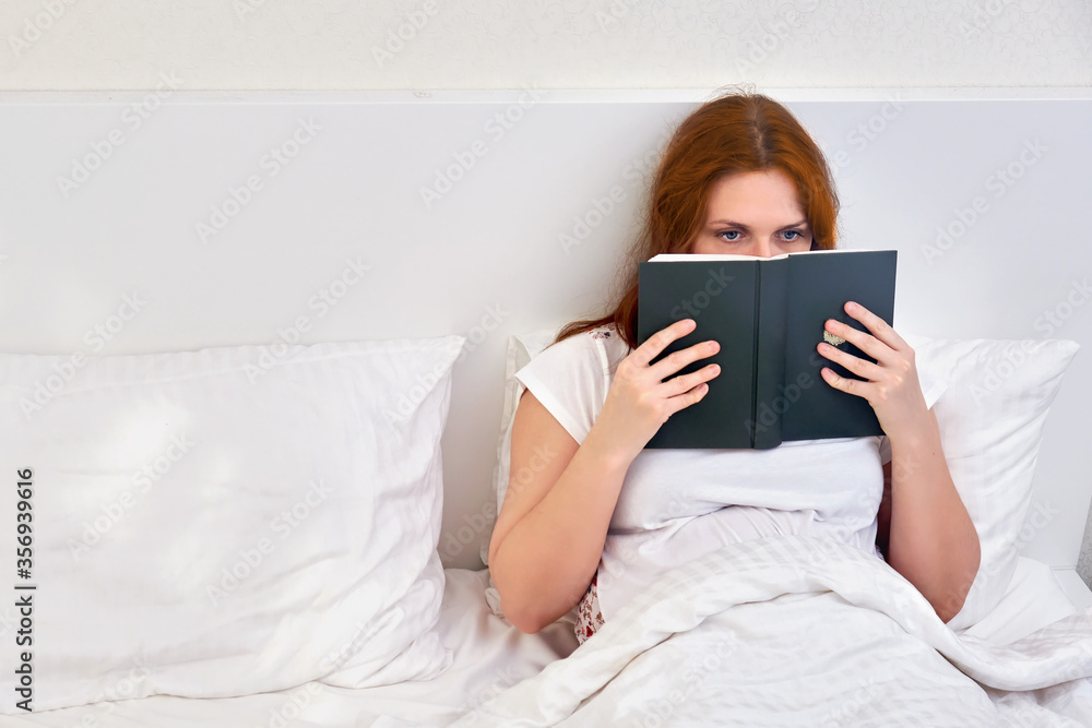 A single woman reads a book lying alone in a double bed. Family relationships in isolation due to coronavirus. A single woman reads a book lying alone in a double bed. Family relationships in isolation due to coronavirus.