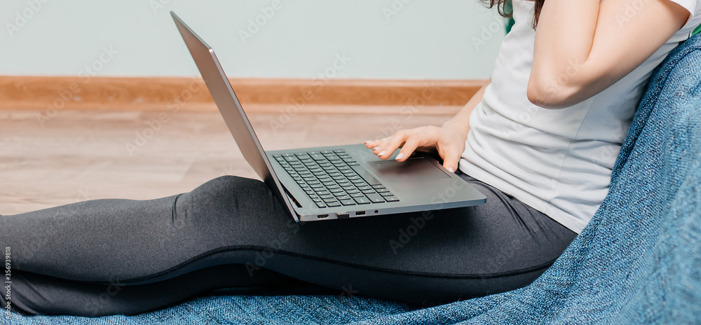 Naklejka premium Girl works on laptop at home. Quarantine. Home spending time during the epidemic. Woman is watching the news. Freelancer.