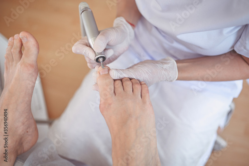 Hardware medical pedicure with nail file drill apparatus. Patient on pedicure treatment with pediatrician chiropodist. Foot peeling treatment at spa with a special device. Clinic of Podiatry Podology