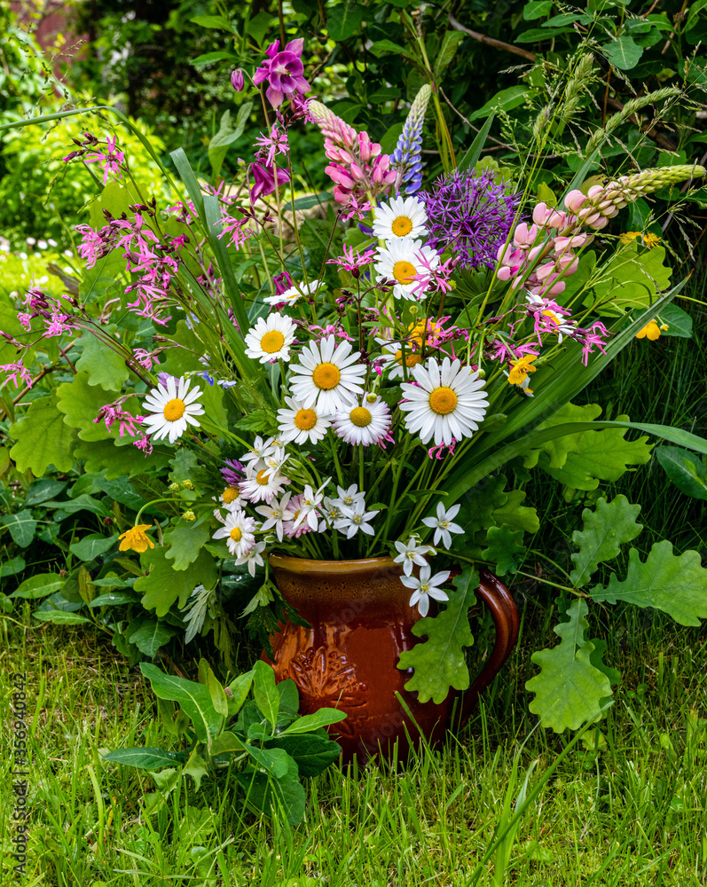 Colorful meadow flower bouquet in a clay mug on a natural background on a sunny day. Summer solstice bouquet in Latvia, Baltics.