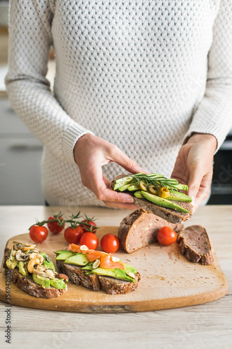 detail of young woman hands making healthy meal of avocado toast and vegetables, indoor natural light, bokeh background
