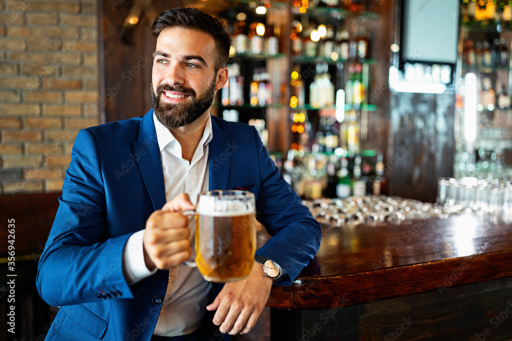 Handsome young man is drinking beer in bar and smiling