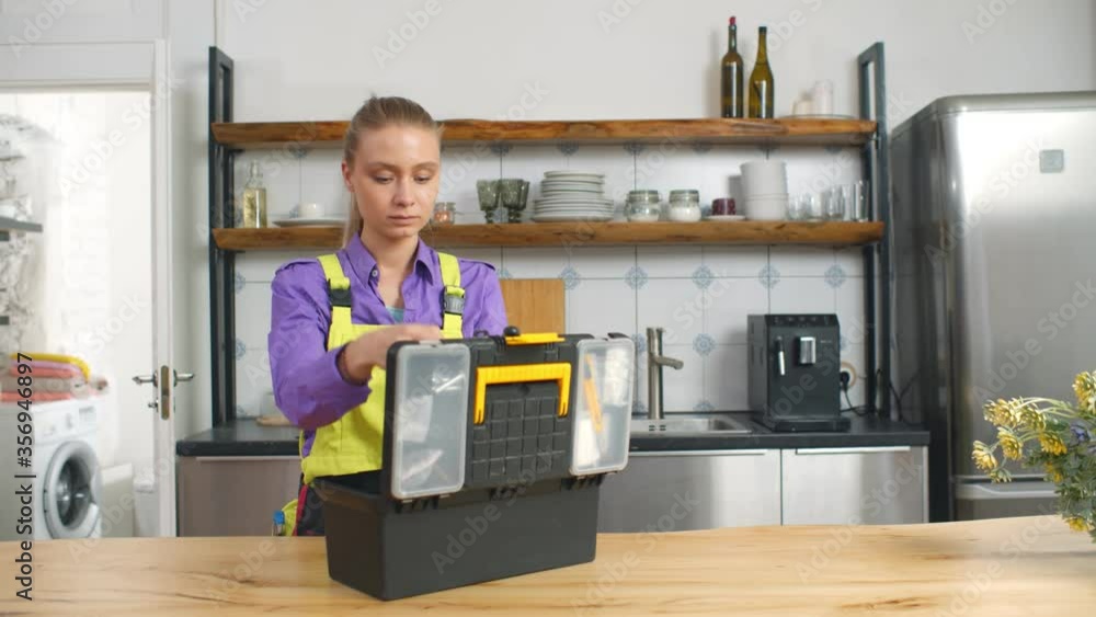 Woman plumber in gloves with toolbox in home kitchen Woman plumber in gloves with toolbox in home kitchen