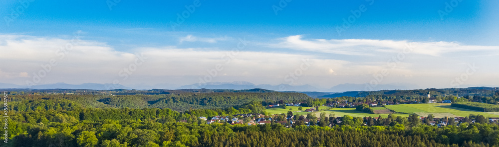 Drone shot of German Bavaria typical town of Buchenhain bird view with Alps in the backround. Forstenrieder Park forest and fields next to town seen from above in spring