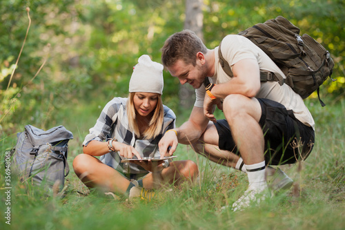 Young hikers sitting on the ground looking at an old map with a compass. Hiking couple in nature. © Nikola Spasenoski