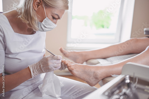 Professional medical pedicure procedure close up using double nail instrument. Patient visiting chiropodist podiatrist. Foot treatment in SPA salon. Podiatry clinic. Pedicurist hands in white gloves.