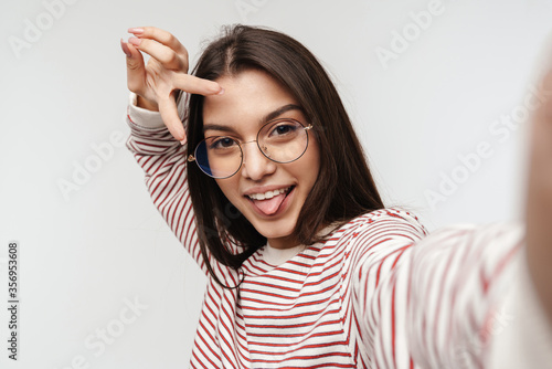 Photo of happy brunette young woman wearing eyeglasses showing peace sign