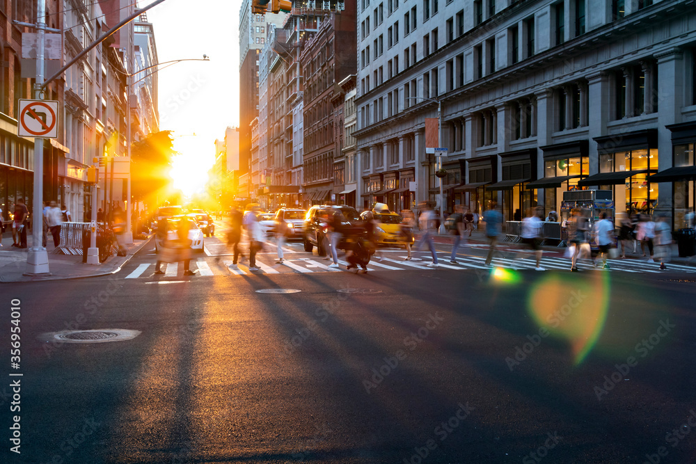 Bright light of sunset shines on the crowds of people crossing a busy intersection on 5th Avenue in Manhattan New York City