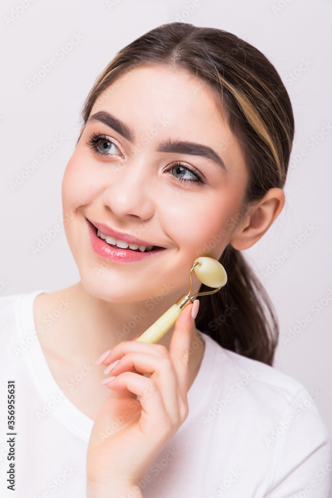 Young beautiful woman is doing a facial massage with a jade roller. Roller massager for smoothing wrinkles on the face. Young beautiful woman is doing a facial massage with a jade roller. Roller massager for smoothing wrinkles on the face.
