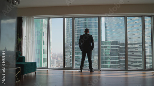Businessman looking at city through window. Successful businessman on the background of skyscrapers. Businessman in office with expensive interior.