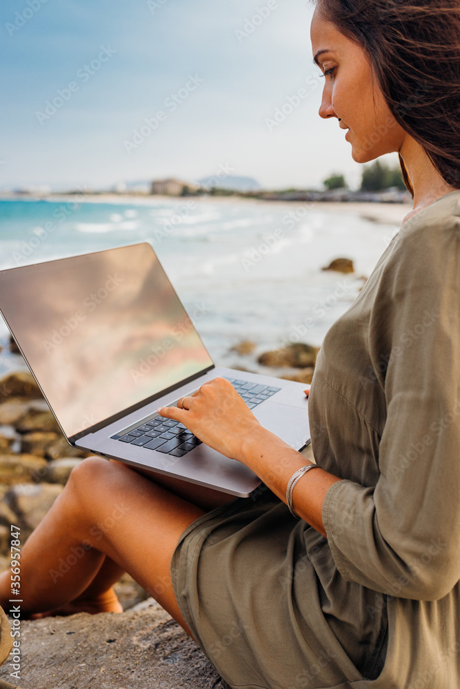 Young pretty female freelancer working on a laptop while traveling by the sea. Using modern technology, the Internet for communication