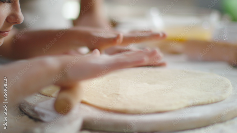 Girl rolling dough on kitchen. Mother and daughter preparing dough at home Girl rolling dough on kitchen. Mother and daughter preparing dough at home