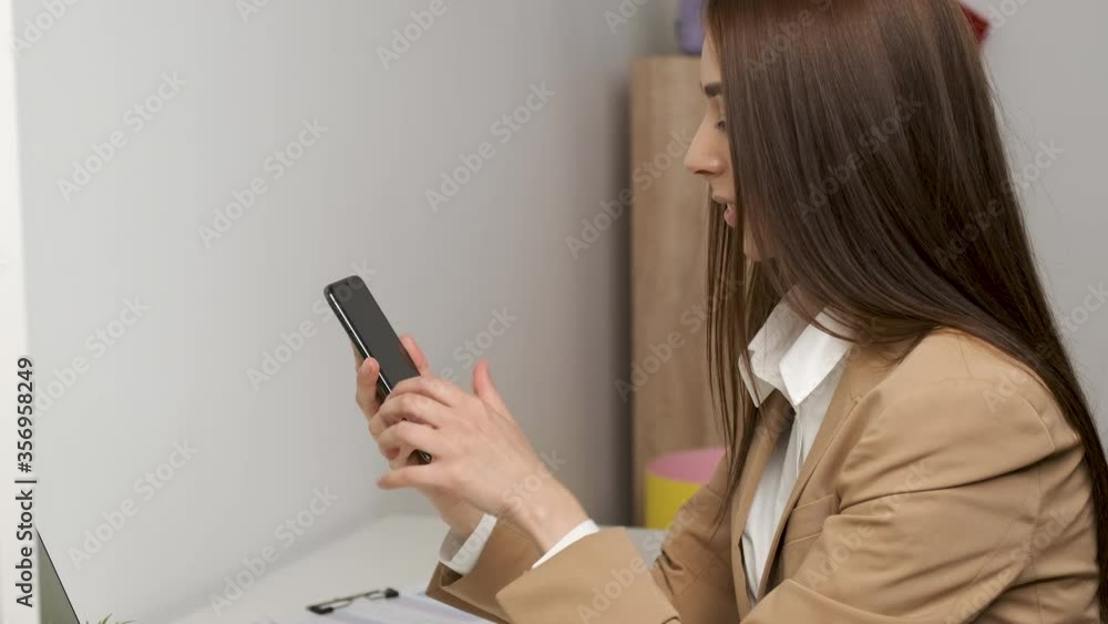 Young beautiful female lawyer working at her workplace holding a phone in her hands and returning to her co-worker with a sincere smile Young beautiful female lawyer working at her workplace holding a phone in her hands and returning to her co-worker with a sincere smile