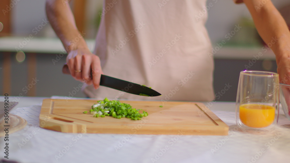 Woman slicing cherry tomatoes on cutting board on kitchen. Girl preparing salad