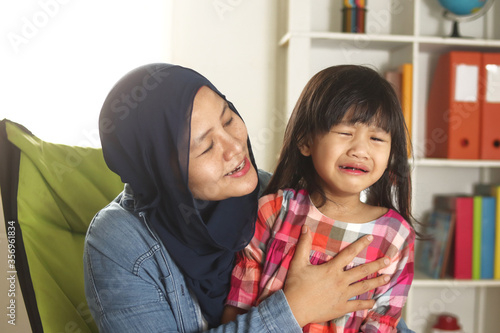 Asian muslim mother hijab calming her sad and crying daughter, single mom and baby girl together