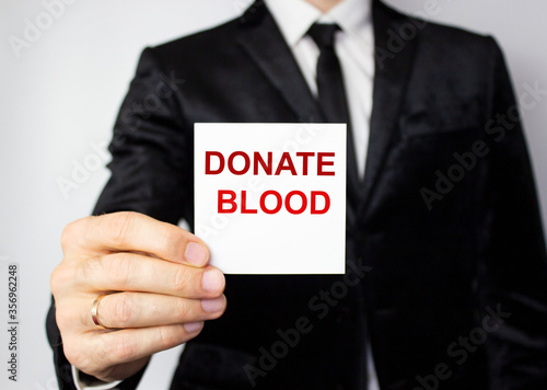 The word blood donation medical concept written in red letters on a white piece of paper in the hands of a businessman.