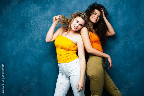 young pretty teenage girls friends with blond and brunette curly hair posing cheerful on blue background, lifestyle people concept © iordani